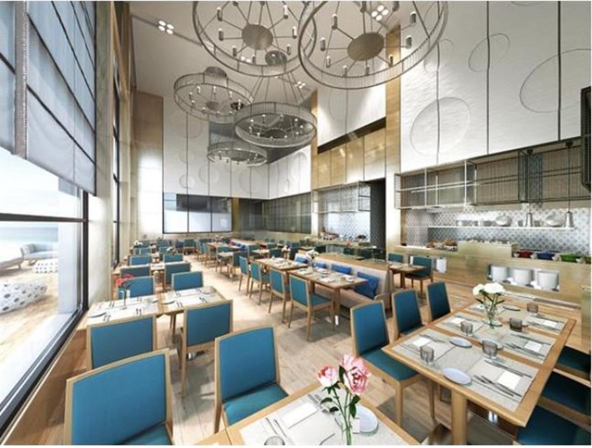 Grand Swiss-Belhotel Waterfront Seef Sanabis Exterior photo The photo depicts a modern restaurant interior featuring a spacious and bright dining area. The decor includes wooden flooring and light wooden furniture, with tables set neatly with blue chairs. Each table has a white tablecloth, plates, cutlery, an
