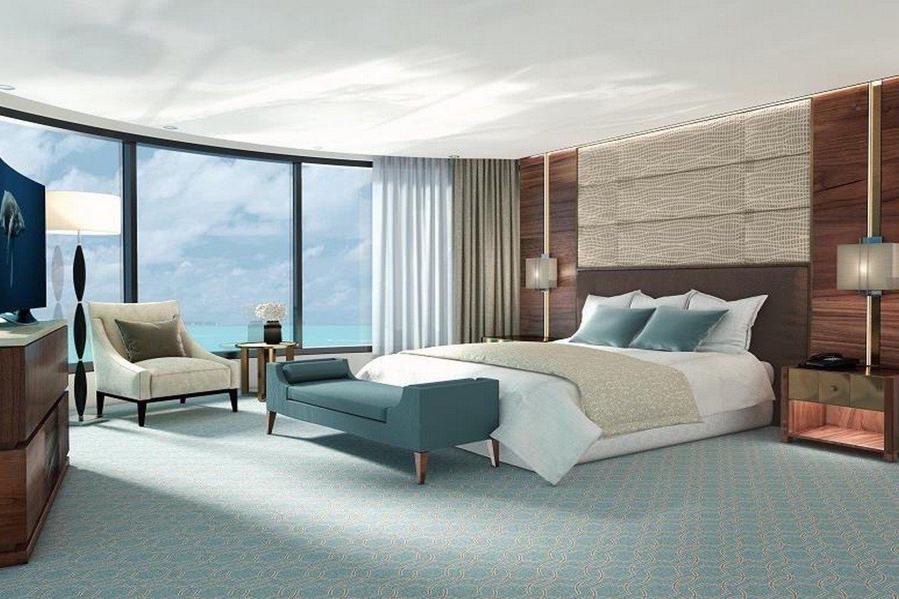 Grand Swiss-Belhotel Waterfront Seef Sanabis Exterior photo The photo shows a modern hotel room with a stylish and contemporary design. It features a large bed with white linens and several light blue accent pillows. On one side of the room, there is a comfortable armchair and a small side table. A sleek, uph