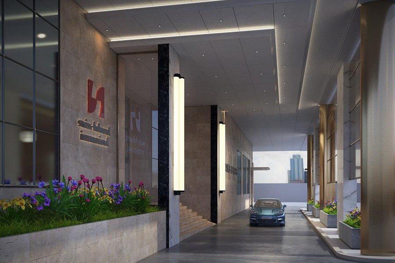 Grand Swiss-Belhotel Waterfront Seef Sanabis Exterior photo The photo shows the entrance of a modern hotel or building. There are tall, sleek columns, with large glass windows on either side. The building features a contemporary design, with an emphasis on clean lines and a polished look. In the foreground, t