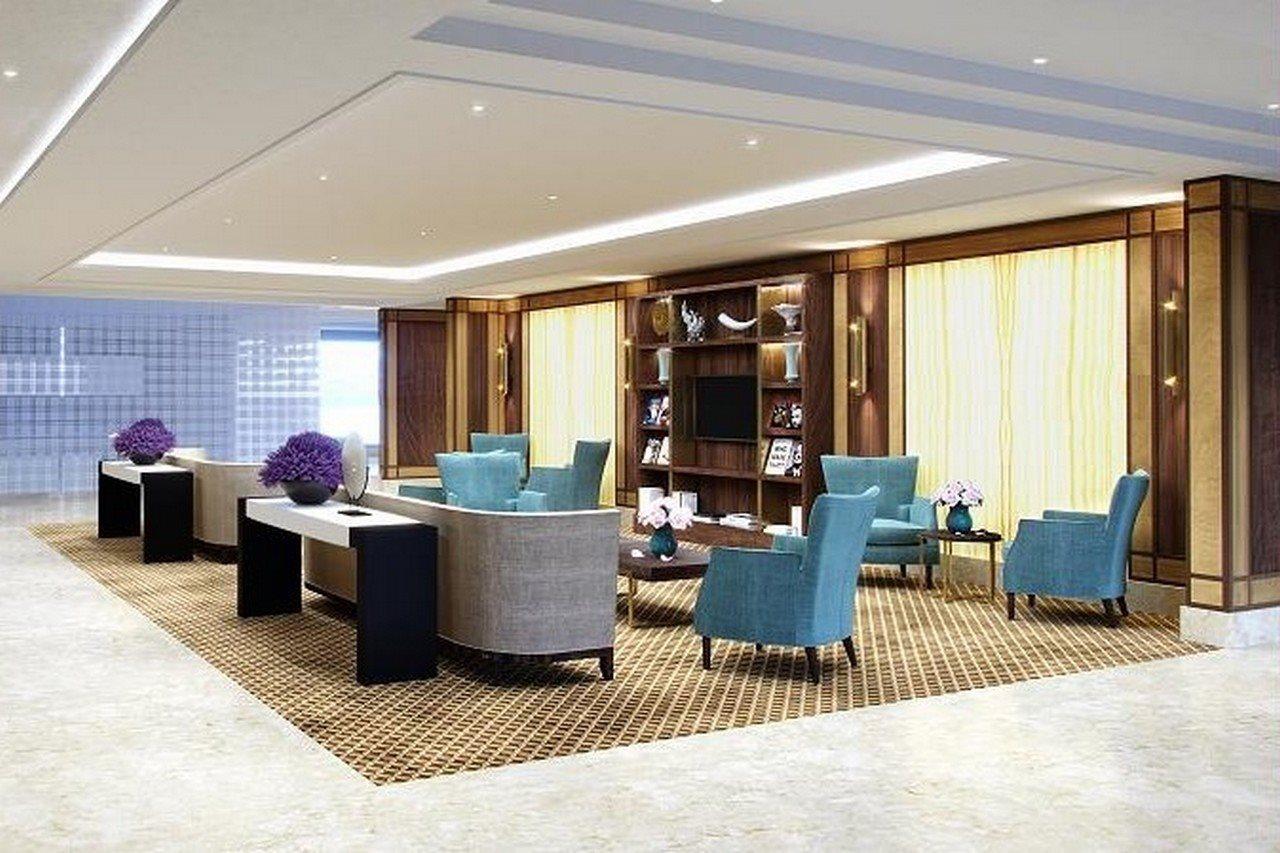 Grand Swiss-Belhotel Waterfront Seef Sanabis Exterior photo The photo shows a modern and elegantly designed lobby or seating area. It has a spacious layout with a combination of light and neutral tones. There are several teal upholstered chairs arranged around a central table. A dark console table is situated
