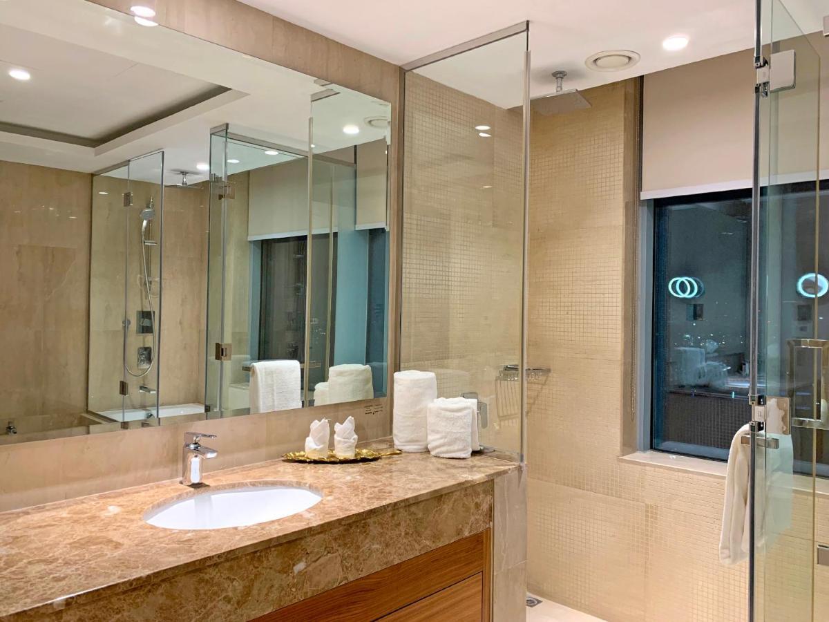 Grand Swiss-Belhotel Waterfront Seef Sanabis Exterior photo The photo shows a modern bathroom designed with a sleek and elegant aesthetic. It features a large vanity with a round sink and a countertop made of marble or a similar stone. The walls and floors appear to be tiled with a light-colored stone, giving