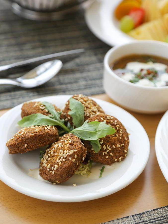 Grand Swiss-Belhotel Waterfront Seef Sanabis Exterior photo The photo shows a plate of golden-brown, fried falafel balls, which are often made from ground chickpeas or fava beans and seasoned with various spices. They are garnished with fresh greens, possibly arugula or similar leafy herbs, and sprinkled with